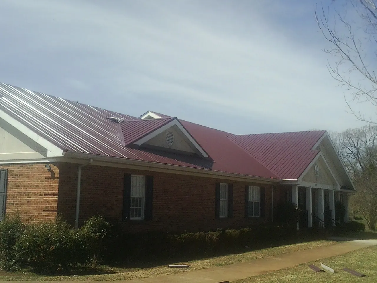Red metal roof with gabled entries on a long brick building, from a Hail Damage Roof Repair job in Normal