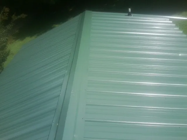 New green metal panels meeting at the ridge of a roof — Flat Roof Repair work by our crew in Normal