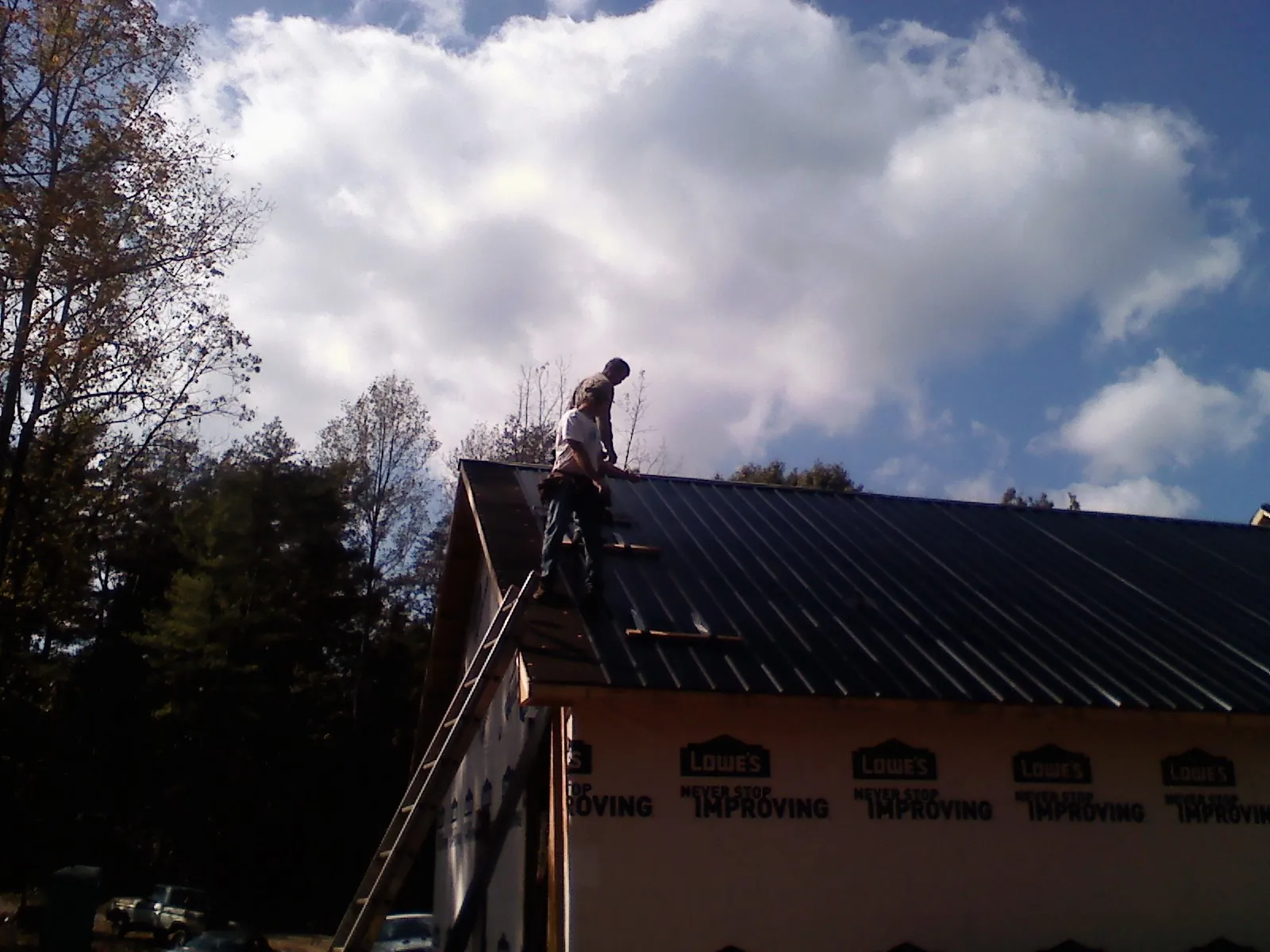 Roofer fastening dark metal panels high against a cloudy sky, from a Roof Inspection job in Normal